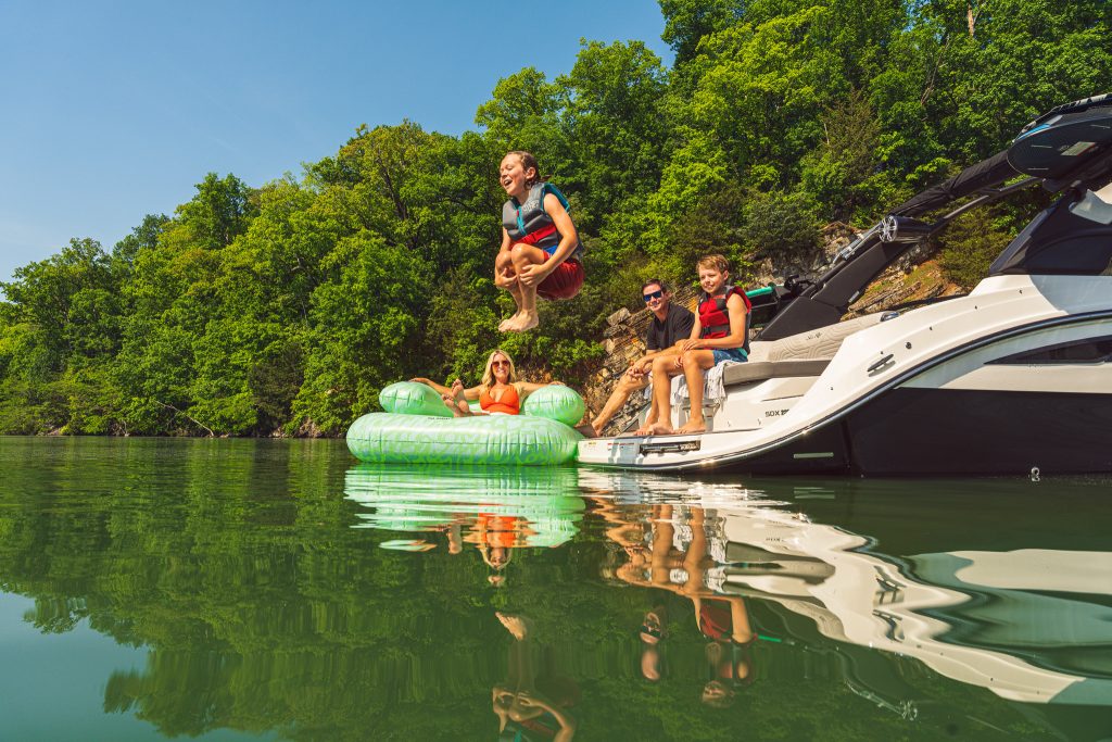 Kid jumping in the water from an SDX 230 Surf while his family watches