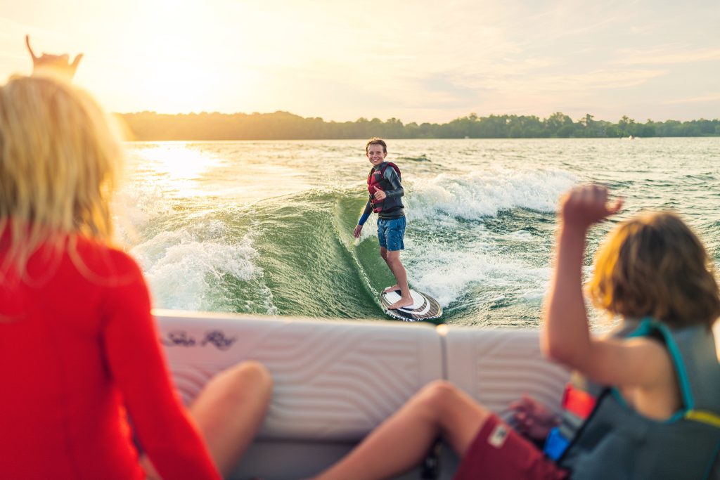 Kid wakesurfing behind an SDX 230 Surf at sunset